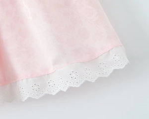 Détail du tissu rose à motifs floraux subtils et ourlet en dentelle florale blanche