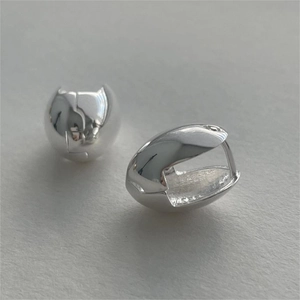 Detailed view of polished silver bean-shaped hoop earrings on a textured gray surface