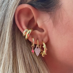 Close-up of bohemian gold earrings with pink zircon heart and lightning charms