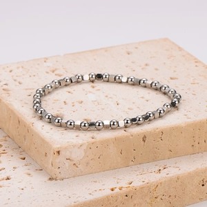 Minimalist silver stainless steel beaded bracelet on a textured beige stone pedestal