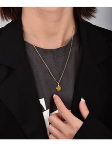 Close-up of a gold necklace featuring a round yellow gemstone pendant on a model