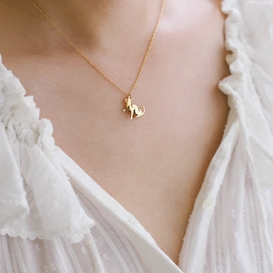 Close-up of a polished gold sitting cat pendant necklace on a white lace shirt