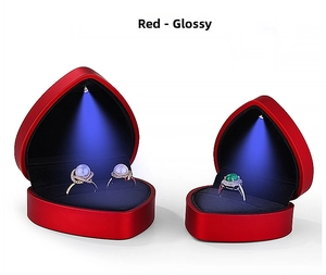 Detail view of red heart jewelry box with LED spotlight illuminating rings on white background