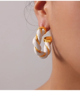 Detailed view of C-shaped hoop earring with twisted gold metal and white leather texture