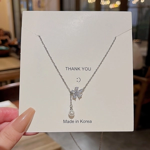 Dettaglio del ciondolo a fiore d'argento con perla su un cartoncino bianco espositivo