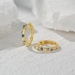 Macro shot of gold star-themed huggie earrings with blue and purple gemstones