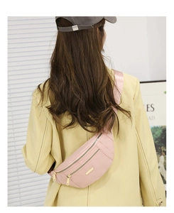 Rear view of a pink nylon crossbody bag with gold zippers worn on a model in a yellow suit