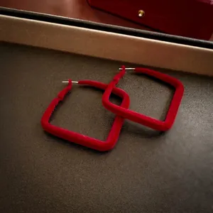 Elegant red flocked square hoop earrings with silver pins on a dark leather tray