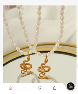 Detail of vintage gold snake pendant with white pearls on a mirrored jewelry tray