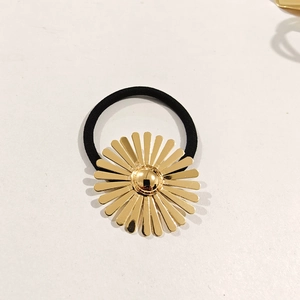 Close-up of golden daisy flower charm on a black elastic hair tie with polished metal finish