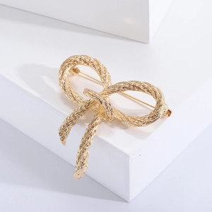 Close-up of golden metal bow brooch with twisted texture on a minimalist stand