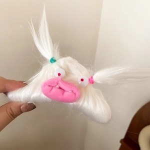 Close-up of white plush monster hair claw clip with funny eyes and pink lips