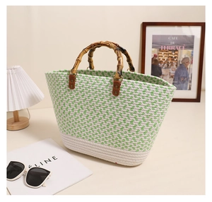 Detail of woven straw handbag featuring green and white patterns and bamboo handles