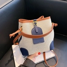 Close-up of a canvas bucket tote bag featuring contrast leather trim and a metal buckle