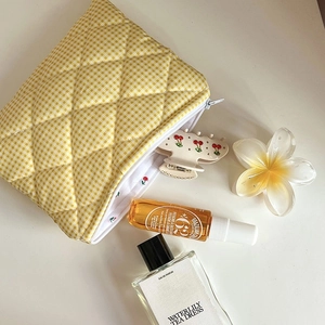 Detailed top view of yellow checkered quilted cosmetic bag with perfume and floral props