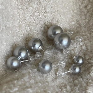 Macro shot of silver-gray pearl stud earrings in various sizes on soft fabric texture