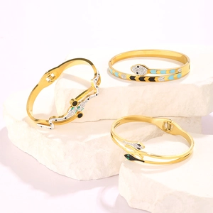 Detail of snake bracelets on stone base featuring gold finish with enamel and gem accents