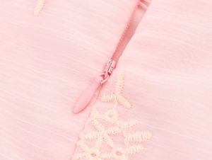 Detail van roze geborduurde stof met verborgen rits en delicate witte bloemmotieven