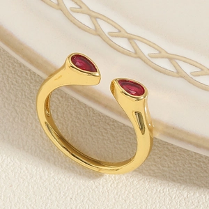 Nahaufnahme goldener Bambus-Ring mit zwei birnenförmigen roten Zirkonia auf weißem Teller
