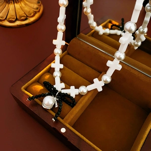 Close-up of pearl necklace featuring a black beaded bow and cross charms on velvet