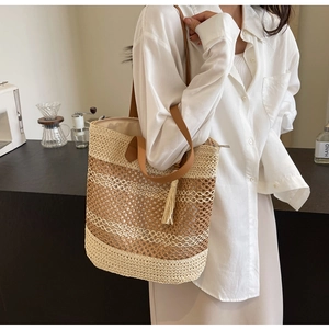 Detail of woven straw beach tote bag with brown leather straps and decorative tassels