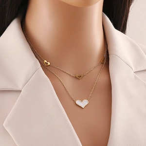 Close-up of a double-layered gold heart necklace with white shell pendant on a model
