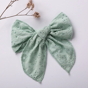 Detail of mint green embroidered cotton bow hair clip with intricate floral cutout patterns