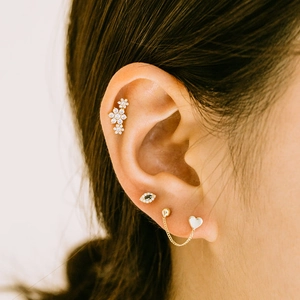 Detail of gold ear piercing set with floral stud, evil eye, and heart drop chain link