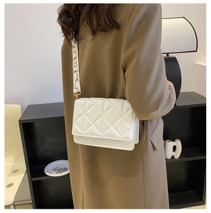 Close-up of white quilted crossbody bag featuring a patterned wide shoulder strap