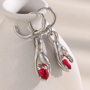 Detailed view of silver hands holding a red heart-shaped gemstone earring on a white vase