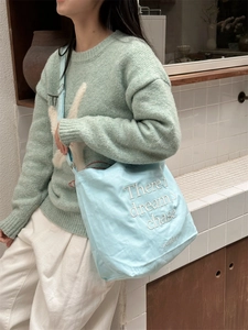 Detail of light blue canvas tote bag with white embroidery and fine shoulder strap