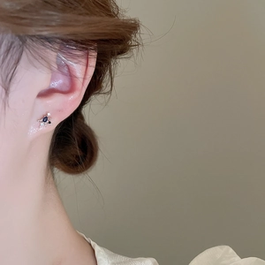 Close-up of heart-shaped silver earrings with blue drop stone on model ear