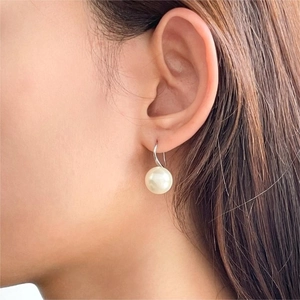 Macro side view of a model wearing minimalist pearl drop earrings with silver hooks