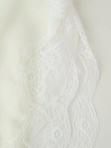 Detailed close-up of intricate white lace embroidery on a smooth satin fabric texture