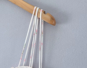 Close-up of thin shoulder straps on a white floral summer dress hanging on wood hanger