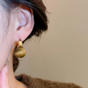 Close-up of golden tiger eye stone earring with heart flower pendant on model's ear