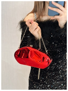 Close-up of a red mirror clutch bag with a gold metal chain against a black dress