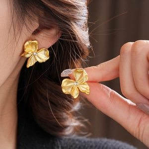 Macro detail of golden flower stud earrings featuring textured petals and a center crystal