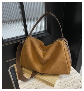 Detail of a brown suede tote bag featuring deep brown leather straps and gold metal hardware