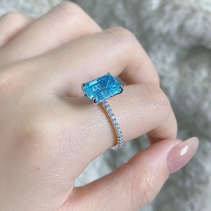 Macro shot of an emerald-cut aquamarine ring on a hand with pavé diamonds