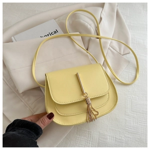 Detail of light yellow PU leather saddle bag featuring metal bar and chain fringe tassels