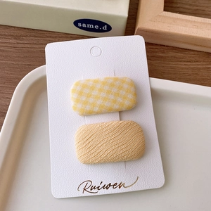 Close-up of yellow plaid and beige wavy fabric hair clips set on a white card display