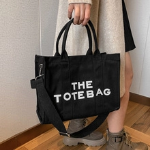 Detail of black canvas tote bag showing the THE TOTE BAG print and adjustable strap