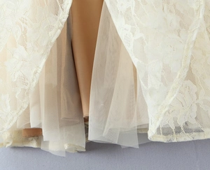 Detail shot of ivory floral lace over beige tulle layers on the sleeveless dress hem