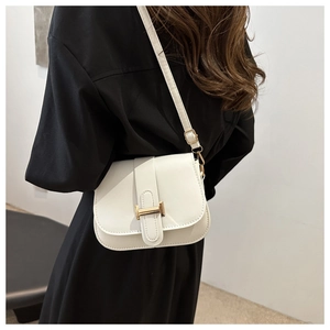 Close-up of white leather crossbody bag with golden H-buckle on black dress