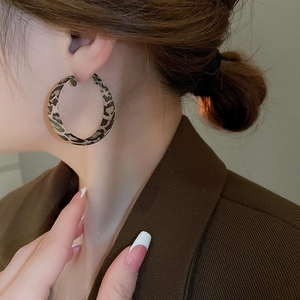 Close-up of a model wearing large leopard print hoop earrings with a brown suit