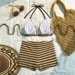 Flat lay of striped two-piece bikini with halter top and high-waisted shorts on white fabric