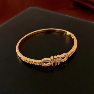 Détail macro d'un bracelet doré ouvert avec boucle style Gancini et zircons incrustés