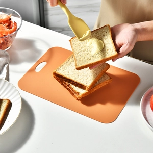 Orange plastic cutting board set being used to spread butter on toast in a modern kitchen