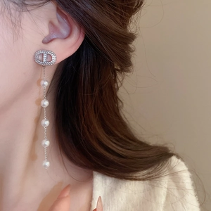 Close-up of elegant silver tassel earrings with CD letters and white pearls on model